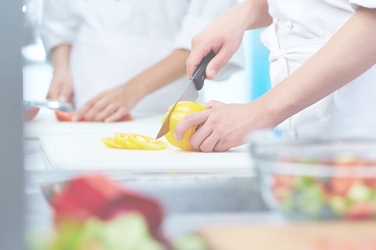 A foodservice employee chops a yellow bell pepper on a cutting board in the kitchen.