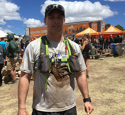 TJ Shields takes a break from running the Ragnar race. He is wearing his sunglasses on the brim of his baseball cap as well as a harness and a soiled T-shirt.